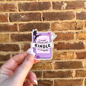 May include: A purple and white sticker with a black silhouette of a dragon and the text "a reader without their KINDLE is a tragedy".