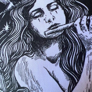 Puede incluir: Un estampado de tela en blanco y negro con una ilustración detallada de una persona con cabello largo y fluido, ojos cerrados, sosteniendo una flauta en los labios. Un pájaro pequeño está posado cerca del cabello y dos estrellas son visibles.