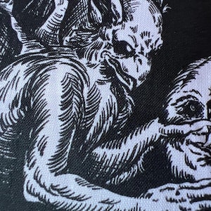 Pode incluir: Uma estampa de tecido em preto e branco com uma ilustração detalhada de uma criatura alada semelhante a uma gárgula, com orelhas pontudas e pele texturizada, estendendo uma mão com garras em direção a um rosto humano com olhos grandes e escuros.