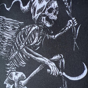 May include: A black fabric surface featuring a white screen-printed graphic of a skeleton wearing a hooded cloak. The skeleton has wings, holds a stalk of wheat in one hand, and grips a curved sickle in the other hand, depicted in a detailed style.