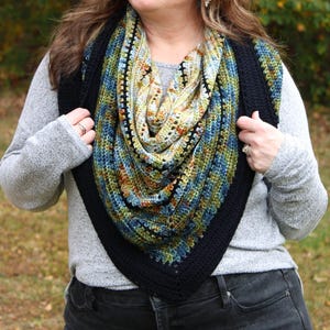 May include: A colourful, crocheted shawl with a black border. The shawl features a mix of blue, green, yellow, and orange hues. The triangular shape is worn around the neck and shoulders, offering a stylish and warm accessory.