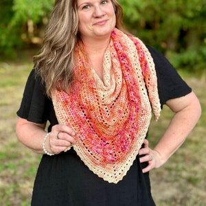 May include: A woman wearing a black dress with a crocheted shawl in shades of peach, orange, and pink.