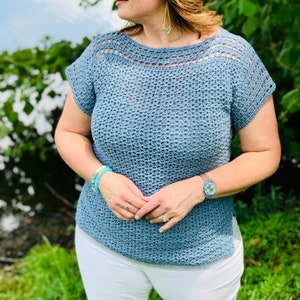 Puede incluir: Un top de crochet azul claro de corte holgado y mangas cortas. El top tiene un escote de crochet y un diseño sencillo.