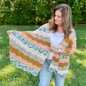 May include: A crochet shawl featuring a wavy, ripple stitch pattern in horizontal stripes of peach, mustard yellow, cream, and variegated blue and green yarn. The lightweight garment has an openwork texture and a scalloped edge design.