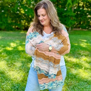 May include: A rectangular crochet shawl featuring a wavy, chevron-inspired pattern in a variegated colour palette of soft peach, warm mustard yellow, cream, and deep teal. The lightweight, open-stitch design creates a delicate, airy texture.