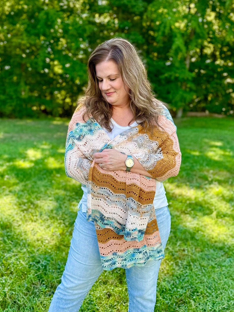 May include: A rectangular crochet shawl featuring a wavy, chevron-inspired pattern in a variegated colour palette of soft peach, warm mustard yellow, cream, and deep teal. The lightweight, open-stitch design creates a delicate, airy texture.