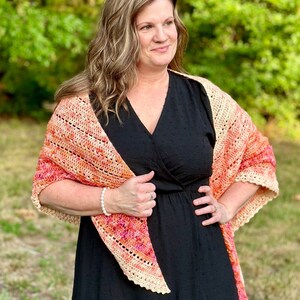 May include: A woman wearing a black dress with a crocheted shawl in shades of orange, pink, and cream. The shawl has a delicate lace edging.