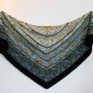 May include: A hand-knitted triangular shawl with a black border and a striped pattern. The shawl features a gradient of colours, including blue, green, and orange, and is made of soft yarn. The shawl is displayed against a white background.