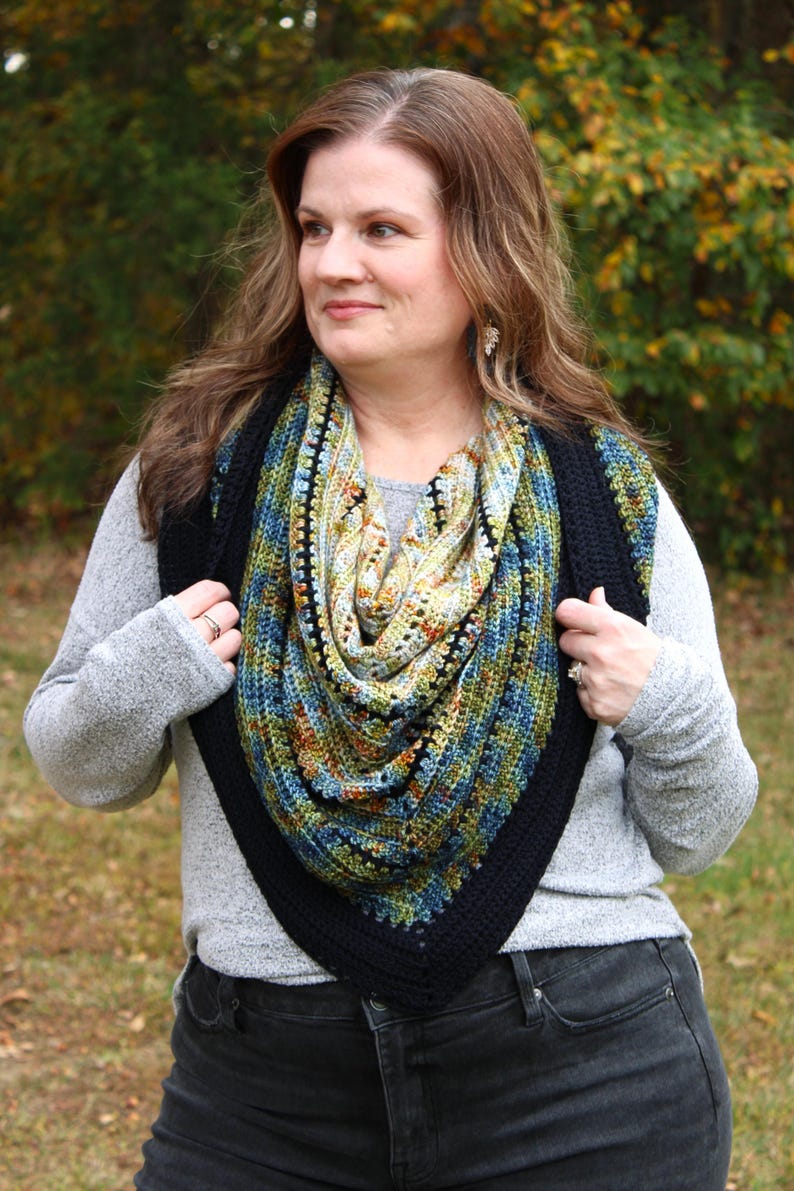 May include: A colourful, crocheted shawl with a black border. The shawl features a mix of blue, green, yellow, and orange hues. The triangular shape is worn around the neck and shoulders, offering a stylish and warm accessory.