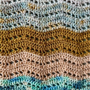 May include: A crocheted fabric featuring a repeating wavy ripple pattern. The design consists of horizontal bands in alternating colours of cream, variegated blue and grey, solid mustard yellow, soft peach, and variegated teal and dark blue.