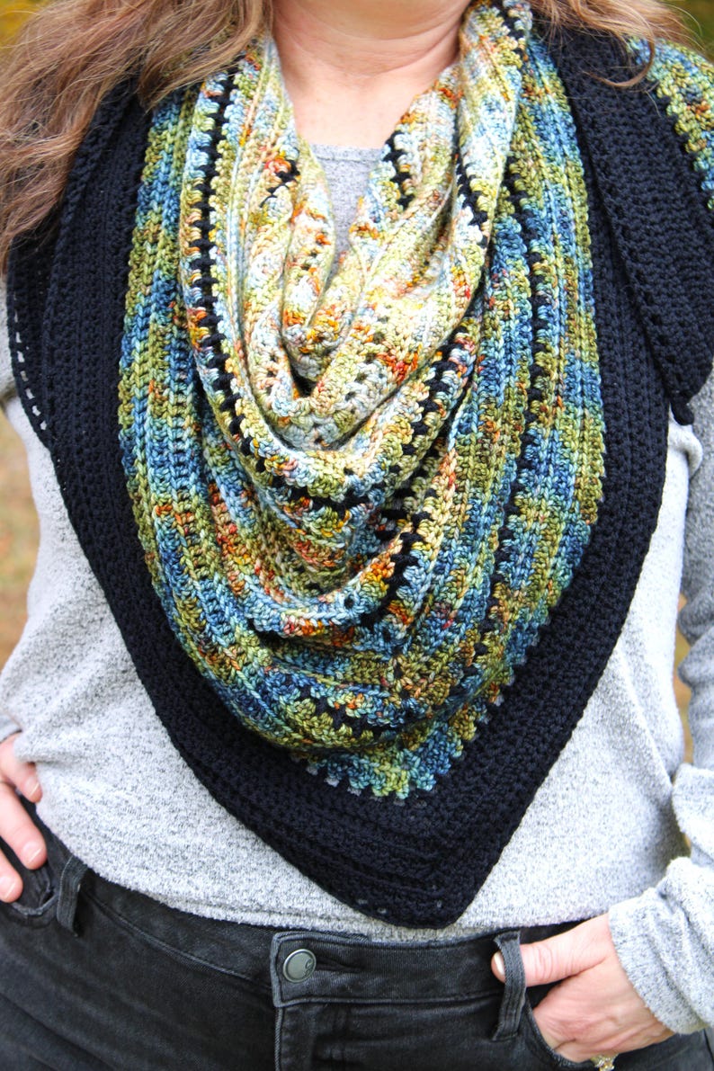 May include: A triangular crochet shawl with a colourful design. The shawl combines blue, green, yellow, and orange hues, framed by a solid black border. The detailed crochet work gives the shawl a textured and attractive appearance.