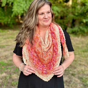May include: A woman wearing a black dress with a crocheted shawl in shades of peach, orange, and pink.