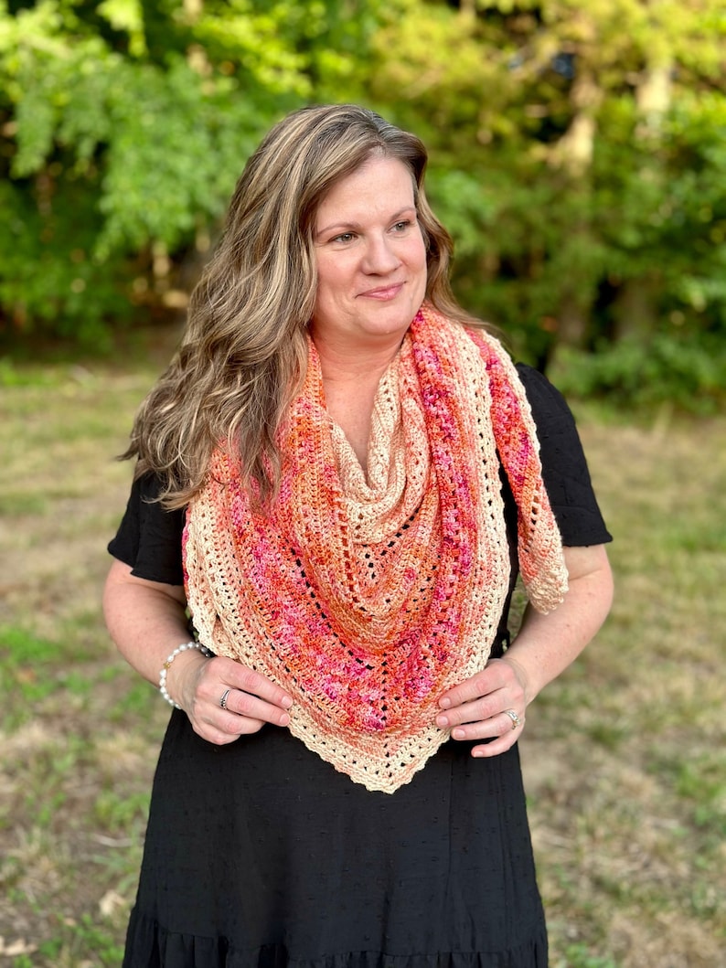May include: A woman wearing a black dress with a crocheted shawl in shades of peach, orange, and pink.