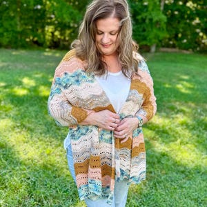 May include: A crochet cardigan featuring a wavy, multi-coloured pattern in shades of mustard yellow, soft peach, cream, and teal blue. The garment has an open front design with a textured, lacy stitch pattern throughout the fabric.