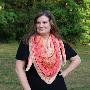 May include: A woman wearing a black dress with a crocheted shawl in shades of pink, orange, and cream. The shawl has a triangular shape and a delicate lace pattern.