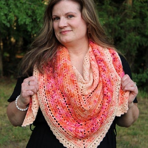 May include: A woman wearing a black dress and a crocheted shawl with a pink, orange, and cream color gradient.