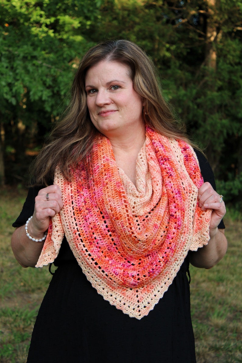 May include: A woman wearing a black dress and a crocheted shawl with a pink, orange, and cream color gradient.