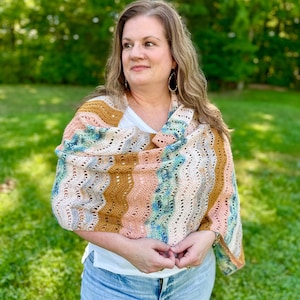 May include: A crochet shawl featuring a wavy, openwork stitch pattern in a variegated colour palette of mustard yellow, soft peach, and speckled blue-green. The rectangular wrap is draped over the shoulders, showcasing a textured yarn construction.