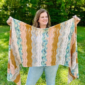 May include: A rectangular crochet shawl featuring a repeating vertical wavy pattern in shades of mustard yellow, soft peach, cream, and variegated teal blue. The textile has an openwork stitch design with visible gaps between the colourful yarn stripes.