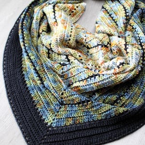 May include: A hand-crocheted shawl in blue, green, yellow, and orange. The shawl features a dark blue border and a textured stitch pattern. The shawl is folded, displaying its intricate design and colour variations. The measurements are in centimeters.
