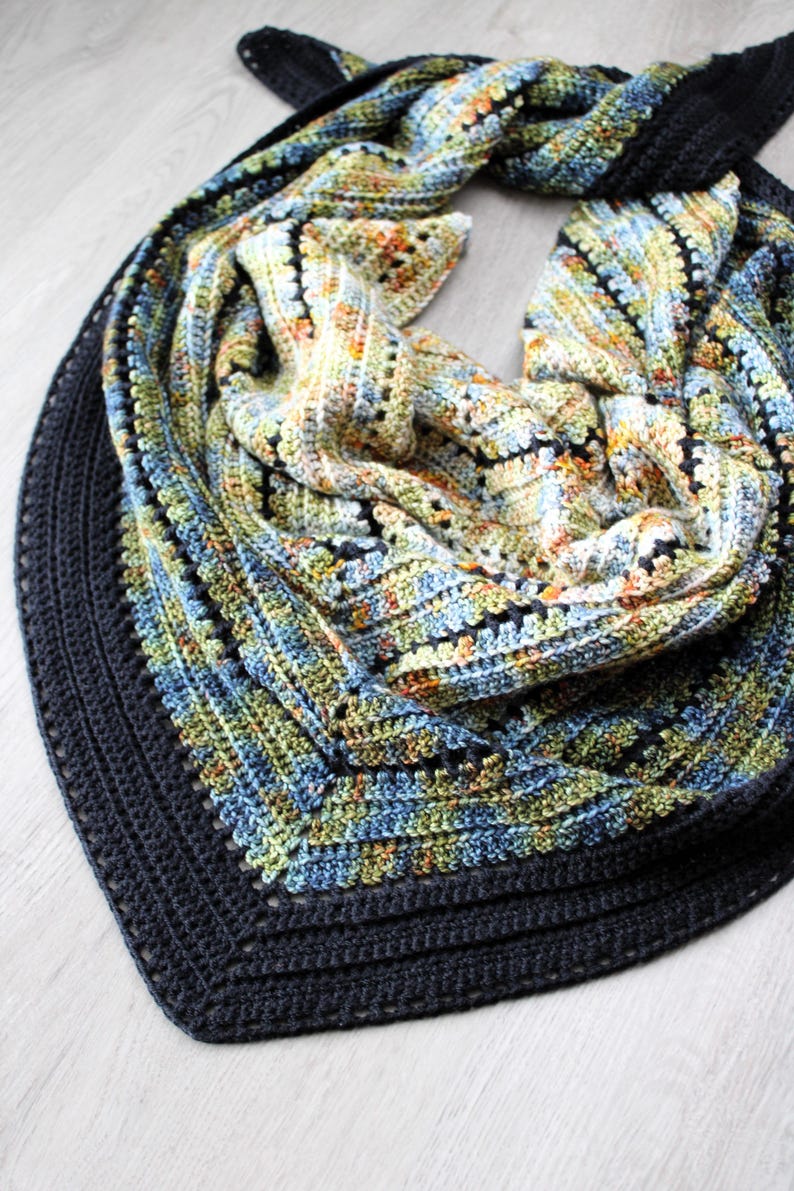 May include: A hand-crocheted shawl in blue, green, yellow, and orange. The shawl features a dark blue border and a textured stitch pattern. The shawl is folded, displaying its intricate design and colour variations. The measurements are in centimeters.