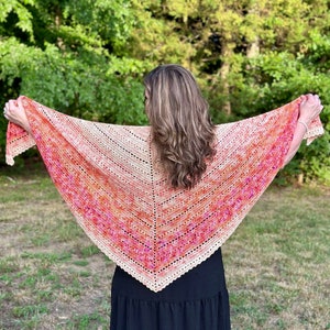 May include: A crocheted shawl with a gradient of peach, pink, and orange colors. The shawl is draped over the shoulders of a person wearing a black dress.