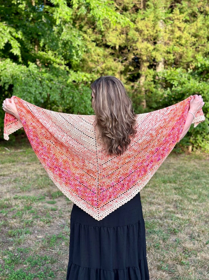 May include: A crocheted shawl with a gradient of peach, pink, and orange colors. The shawl is draped over the shoulders of a person wearing a black dress.