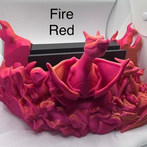 Könnte beinhalten: Ein 3D-gedruckter Nintendo Switch-Dock-Ständer mit einem pinkfarbenen Glurak und anderen Pokémon-Charakteren in einem feurigen Design. Der Text "Fire Red" ist im Hintergrund sichtbar.