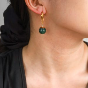 May include: Gold hoop earrings with a dangling green stone bead.