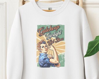 Puede incluir: Sudadera blanca con el texto "Gatekeep Gaslight Girl Boss" y una ilustración de estilo vintage de una mujer flexionando el brazo. El gráfico presenta a una mujer con camisa azul y pañuelo rojo.