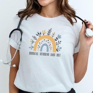 Könnte beinhalten: Ein weißes T-Shirt mit einem Regenbogen- und Blumenmuster. Der Text "Neonatal Intensive Care Unit" ist unter dem Design gedruckt.