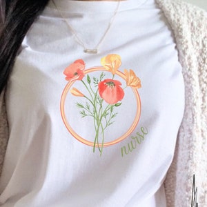 Könnte beinhalten: Weißes T-Shirt mit einem Aufdruck von orangefarbenen und roten Blumen in einem Kreis mit dem Wort "nurse" im Kreis.