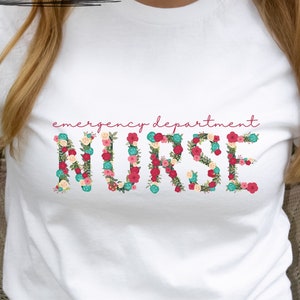 Könnte beinhalten: Weißes T-Shirt mit den Worten "emergency department nurse" in rosa Schrift. Das Wort "nurse" besteht aus bunten Blumen.