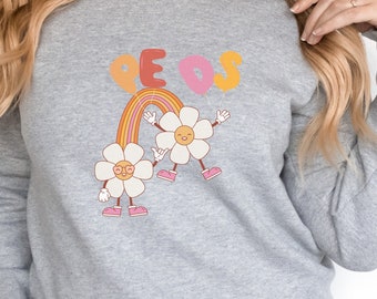 Puede incluir: Una sudadera gris con un arcoíris y dos margaritas sonrientes con la palabra "Peace" en letras de arcoíris encima.