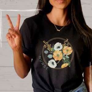 Könnte beinhalten: Schwarzes T-Shirt mit einem Blumendesign und dem Wort "NURSE", das vertikal auf der linken Seite des Designs gedruckt ist.