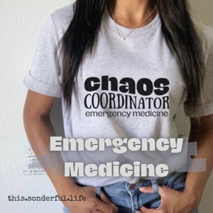 May include: A gray t-shirt with black text that reads "chaos coordinator emergency medicine".