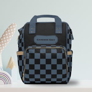 May include: A black and blue checkered diaper bag with a gold zipper and a name tag that says "CAMERON GREY".