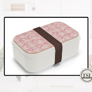 May include: A white lunch box with a pink and white bow pattern and a brown strap.