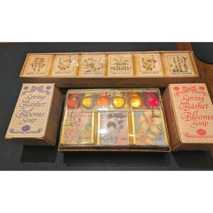 May include: A selection of vintage bath products, including a box of six floral-themed bath cubes and two boxes of "Spring Basket of Blooms Soap." The bath cubes feature illustrations of flowers and the soap boxes have a floral design.
