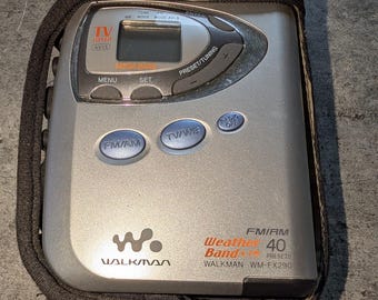 May include: A silver Sony Walkman WM-FX290 portable radio with a black protective case. The device features a digital display, FM/AM and TV/WB buttons, and text reading Weather Band, 40 Presets, and Walkman. It has a compact, rectangular design.