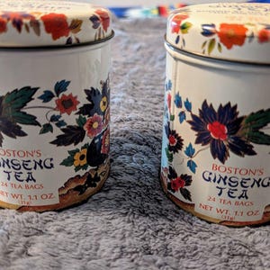 May include: Two white metal tea tins with blue and red floral designs. The tins contain Boston's Ginseng Tea with 24 tea bags and a net weight of 1.1 ounces.