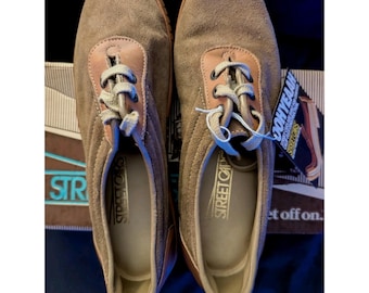 May include: Pair of brown suede Street Cats sneakers with tan leather accents. The shoes have light-colored laces and are displayed on a brown box. The brand name is visible on the side of the shoe and on the box.