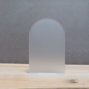 May include: A frosted acrylic display stand with an arched top. The stand is clear and has a smooth, matte finish.