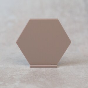 May include: A light brown hexagonal display stand with a flat top surface. The stand is made of a smooth material and has a simple, modern design.