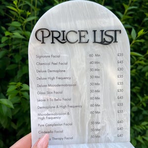 Puede incluir: Una lista de precios con un patr&oacute;n de m&aacute;rmol blanco y gris con texto negro. El texto en la parte superior dice "LISTA DE PRECIOS", seguido de una lista de tratamientos faciales, duraciones y precios. Los tratamientos incluyen "Signature Facial" y "Cinderella Facial".