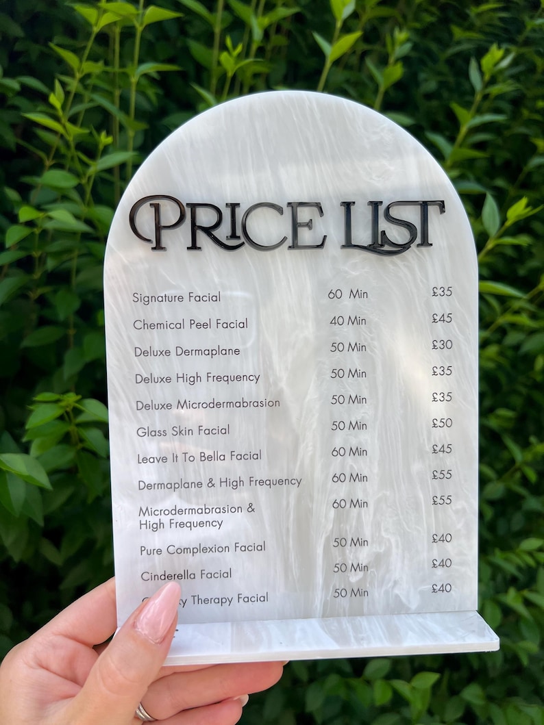 Puede incluir: Una lista de precios con un patr&oacute;n de m&aacute;rmol blanco y gris con texto negro. El texto en la parte superior dice "LISTA DE PRECIOS", seguido de una lista de tratamientos faciales, duraciones y precios. Los tratamientos incluyen "Signature Facial" y "Cinderella Facial".