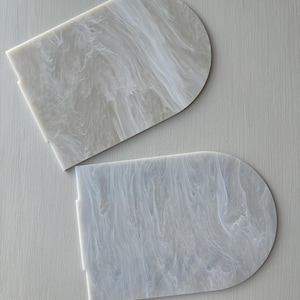 Puede incluir: Dos posavasos semicirculares de acr&iacute;lico blanquecino con efecto marmolado. Los posavasos tienen una base rectangular plana y una parte superior redondeada. El patr&oacute;n arremolinado crea un aspecto &uacute;nico y elegante.