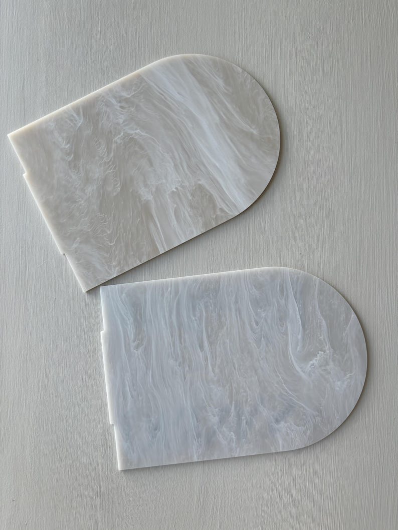 Puede incluir: Dos posavasos semicirculares de acr&iacute;lico blanquecino con efecto marmolado. Los posavasos tienen una base rectangular plana y una parte superior redondeada. El patr&oacute;n arremolinado crea un aspecto &uacute;nico y elegante.