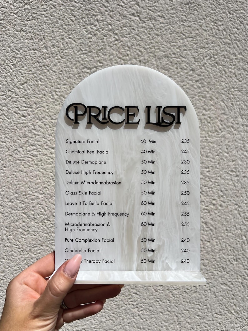Puede incluir: Una lista de precios de acr&iacute;lico blanco y negro veteado con una parte superior curvada. El texto negro dice "PRICE LIST" encima de una lista de tratamientos faciales, incluyendo Signature Facial y Chemical Peel Facial.