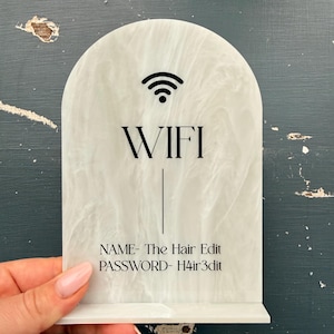 May include: White marble-effect acrylic WiFi sign with black text. The sign has a rounded top and a base for standing. It displays a WiFi symbol, the word "WIFI", and the network name and password: "The Hair Edit" and "H4ir3dit".